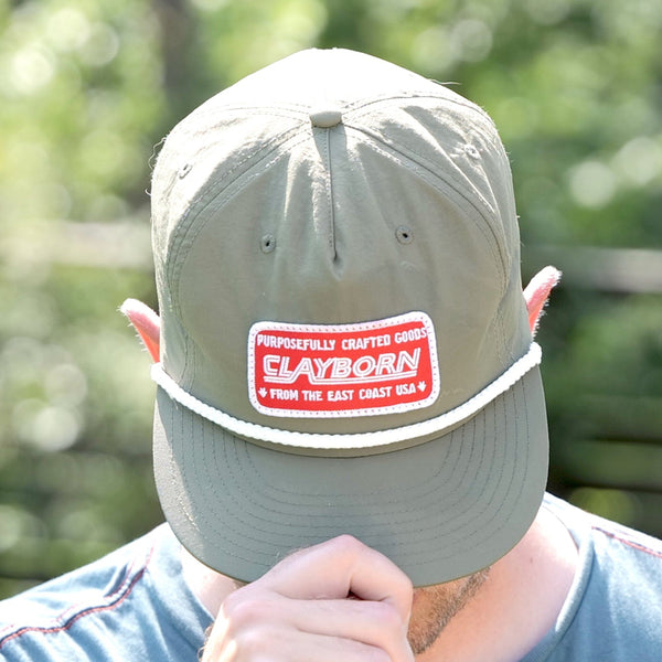 Person holding a Clayborn Surf cap with a visible brand logo in a natural setting