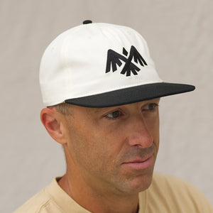 Alpine Crow Snapback Hat with a white crown and black bill on the head of a man looking to the side. 